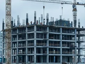 A multi-storey reinforced concrete building under construction, with tower cranes overhead and a site team in high-visibility vests.